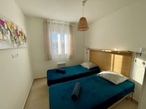 Bright bedroom with two twin beds, teal bedding, wooden headboard, wicker pendant light at Marina di Bravone hotel,