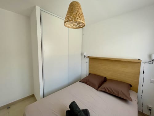 Chambre moderne à la Résidence Marina di Bravone avec tête de lit en bois, luminaire suspendu tressé et armoire blanche à Linguizzetta