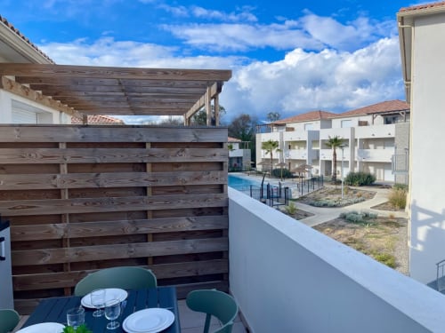 Balcon de l'appartement Marina di Bravone avec pergola en bois, vue sur la piscine et bâtiments modernes blancs à Linguizzetta