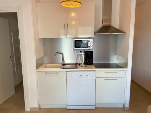 Kitchenette moderne dans l'appartement Marina di Bravone avec placards blancs, crédence en acier inoxydable, évier et lave-vaisselle