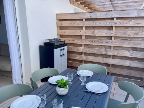 Coin repas à Marina di Bravone : table foncée, chaises menthe, couverts dressés et terrasse en bois