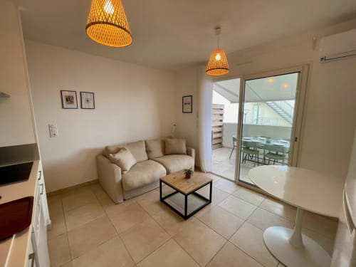 Salon moderne de la Résidence Marina di Bravone avec canapé beige, table basse en bois et accès à la terrasse vue mer