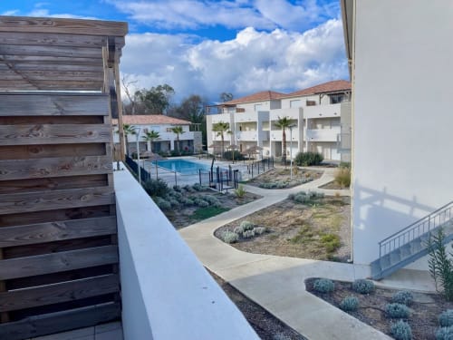 Cour de la Résidence Marina di Bravone avec piscine, appartements blancs, palmiers et ciel bleu à Linguizzetta