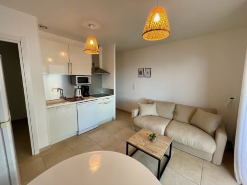 Appartement moderne à la Résidence Marina di Bravone avec kitchenette, canapé beige, luminaires suspendus et décor côtier