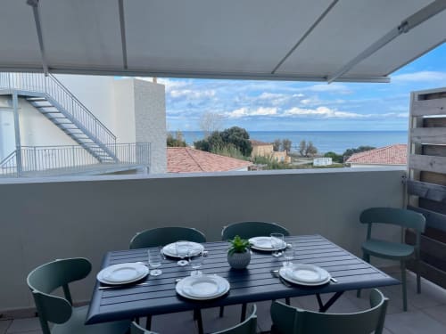 Terrasse bord de mer à la Résidence Marina di Bravone avec table dressée, store rétractable et vue sur la Méditerranée