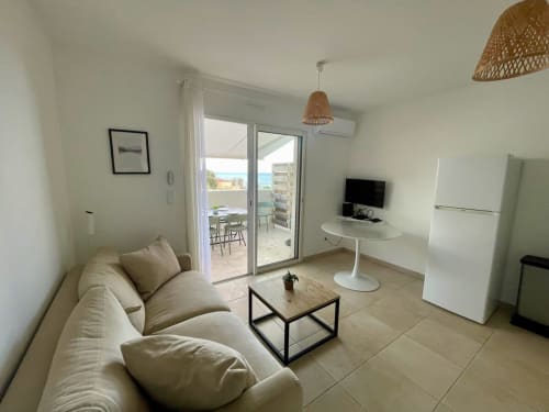 Appartement T3 moderne à la Résidence Marina di Bravone avec vue mer, canapé beige, TV et accès terrasse à Linguizzetta