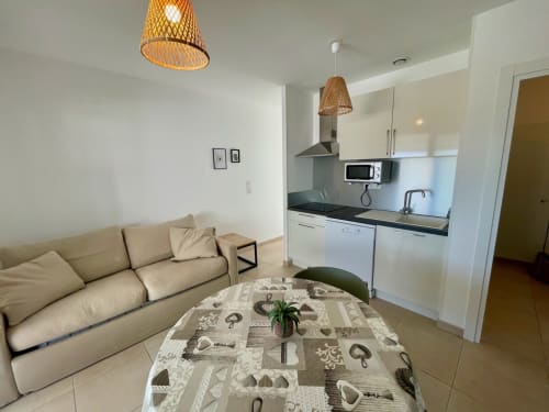 Moderno appartamento T3 a Résidence Marina di Bravone con divano beige, cucina attrezzata, lampade a sospensione intrecciate e stile costiero