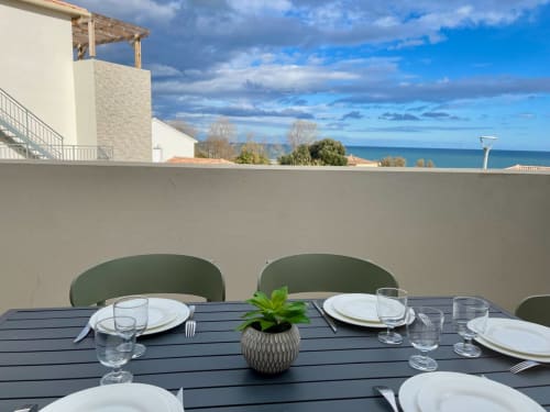 Terrazza esterna con tavolo preparato, sedie verdi e vista sul mare a Marina di Bravone