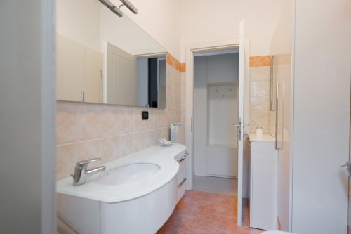 Moderno bagno nell'appartamento Perla Marina a Finale Ligure, con lavabo bianco, specchio, pareti piastrellate e zona doccia