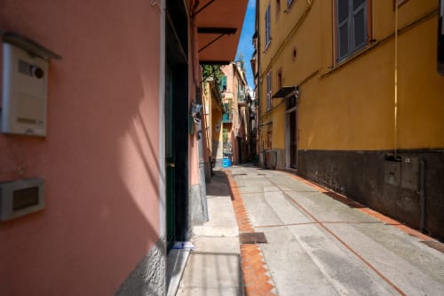 Strettissima via colorata a Varigotti, Finale Ligure con edifici rosa e gialli e strada piastrellata