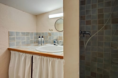Salle de bains moderne du gîte Lavande au Domaine Bellavigne avec lavabo blanc, miroir rond, douche en carrelage marron et décoration épurée