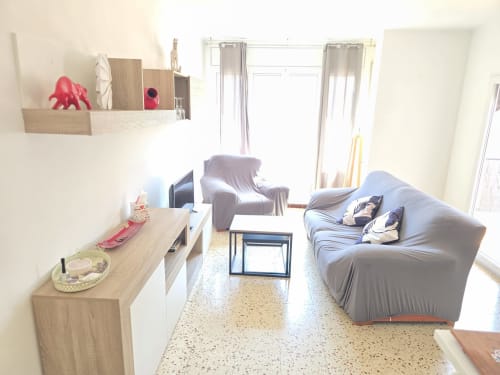 Modern living room in family apartment in Rosas with gray sofa, wooden furniture, TV, and glass doors opening to balcony