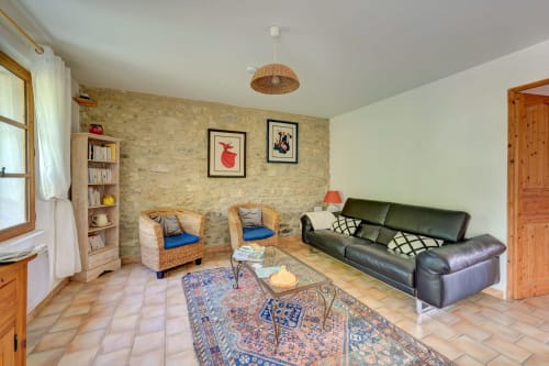 Spacieux séjour du gîte Romarin au Domaine Bellavigne avec fauteuils en osier, canapé foncé, murs en pierre et jardin