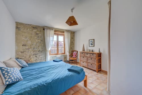 Chambre lumineuse au gîte Romarin du Domaine Bellavigne avec literie bleue, mur en pierre, fenêtre sur jardin