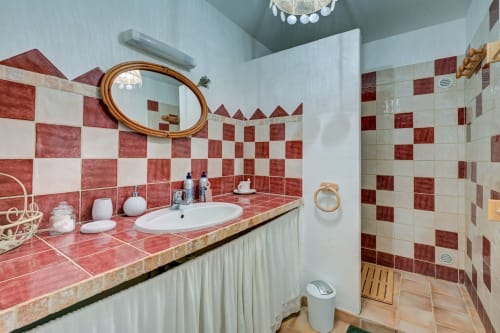Salle de bain moderne du gîte Romarin avec carrelage à damier rouge et blanc, miroir ovale et douche à l'italienne