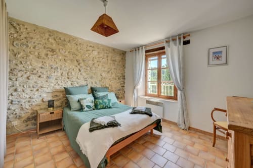 Chambre lumineuse du Gîte Romarin au Domaine Bellavigne avec mur en pierre, literie verte, meubles en bois et jardin
