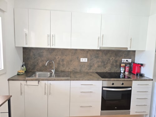 Modern white kitchen with dark countertops and backsplash, stove, sink, and cabinets in Rosas apartment