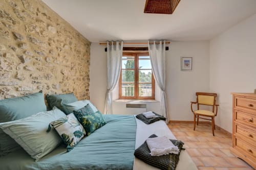 Chambre spacieuse à la Gîte Romarin du Domaine Bellavigne avec mur en pierre, literie bleue, mobilier en bois et jardin