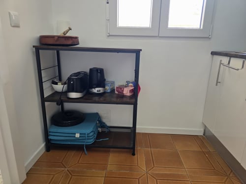 Utility shelf in apartment kitchen with appliances, storage items, and blue quilted bags on lower shelf