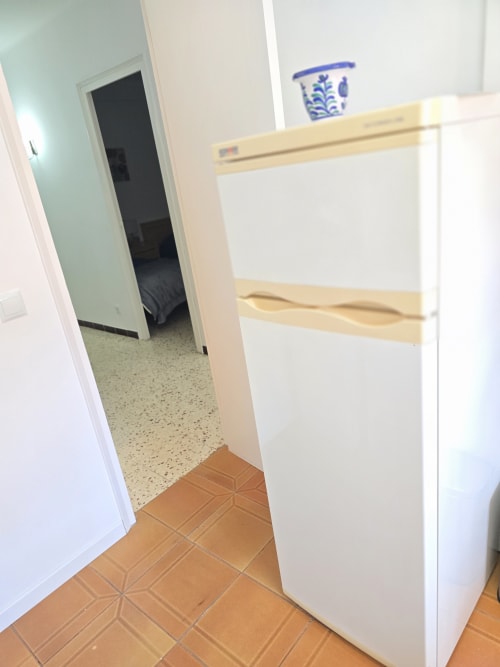 Kitchen hallway in Rosas apartment with white cabinets, wooden shelves, and terracotta tile flooring