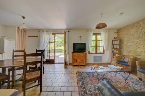 Spacieux séjour ouvert au Gîte Romarin du Domaine Bellavigne avec table à manger, TV, fauteuils en osier, pierre