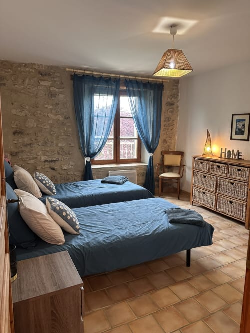 Chambre spacieuse avec deux lits bleus, murs en pierre et vue sur le jardin au Domaine Bellavigne Gîtes, Forcalquier
