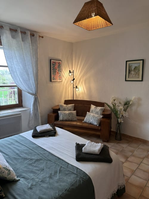 Chambre accueillante au gîte Romarin avec canapé bois, lampe plafond tressée, vue jardin et équipements modernes