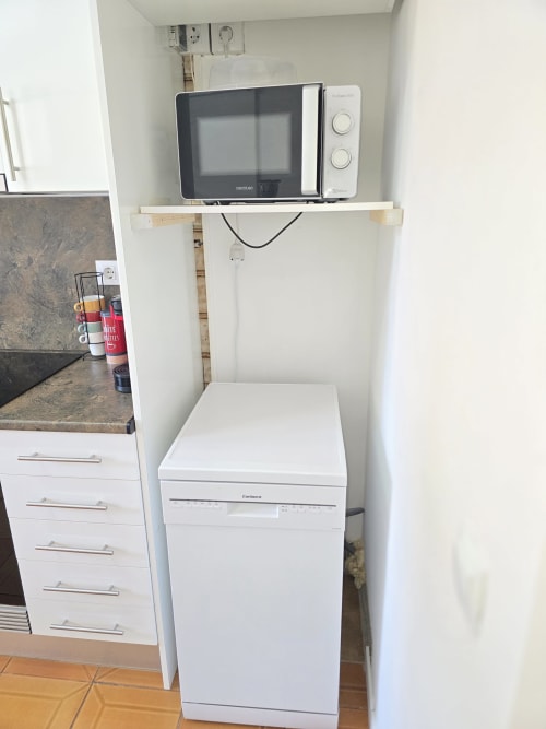 Compact kitchen corner with microwave on shelf, white appliances and drawers in Rosas apartment