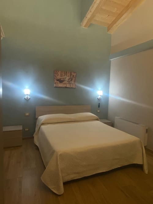 Camera moderna di Villa Maria con letto matrimoniale, pareti verde salvia, travi in legno e applique a Roggiano Gravina