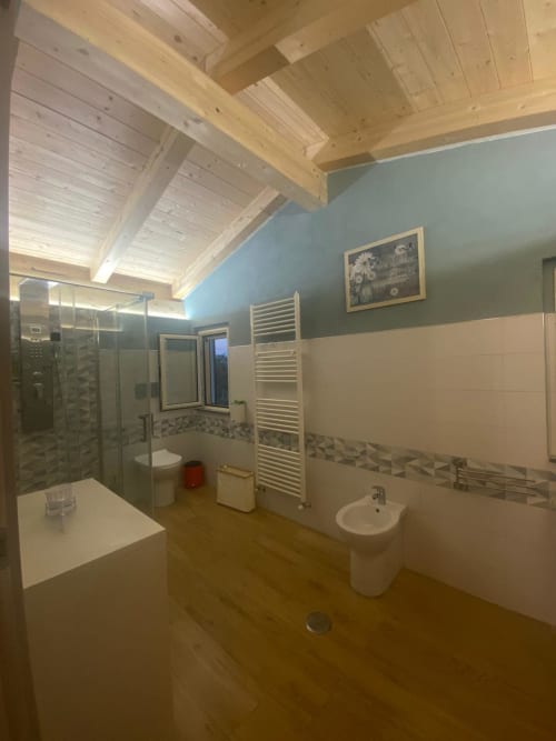 Bagno moderno di Villa Maria con soffitto a travi di legno, pareti blu superiori, pareti bianche inferiori, doccia in vetro, lavabo a colonna