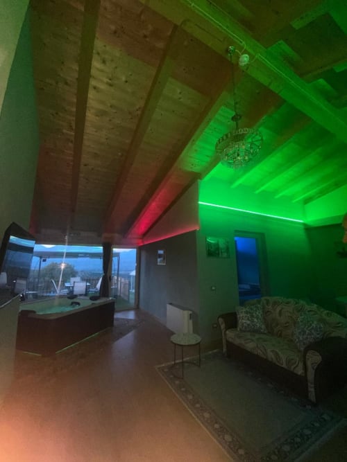 Interno moderno dell'appartamento a Villa Maria con luci LED al soffitto verde neon e rosa, travi in legno a vista, area cucina e