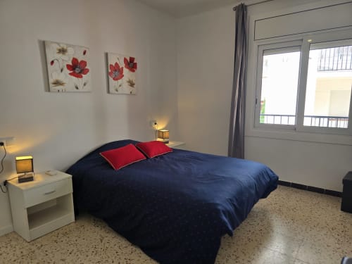 Modern bedroom in Rosas apartment with navy bed, red pillows, floral wall art, and balcony access to city views