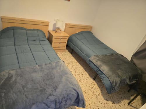 Twin beds with blue comforters in Rosas apartment bedroom, wooden nightstand and beige tiled floor