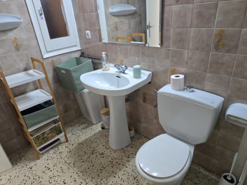 Bright bathroom in Rosas apartment with pedestal sink, toilet, tile walls, and wooden storage shelf