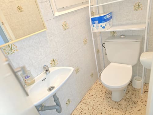 Modern bathroom with white sink, toilet, and decorative tiled walls in Rosas apartment rental with city views.