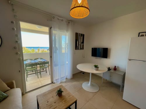Marina di Bravone T2 apartment with sea view, dining table, kitchenette, and balcony overlooking beach