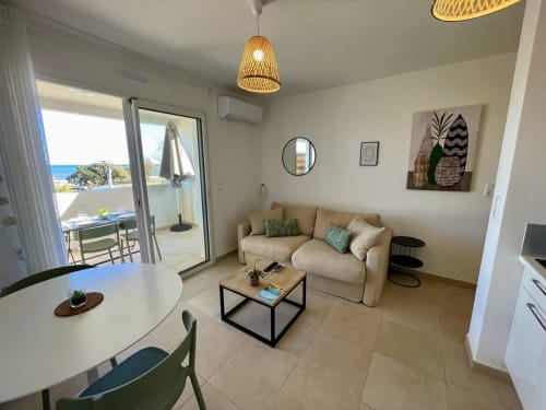 Soggiorno moderno della Résidence Marina di Bravone con divano beige, tavolo da pranzo e balcone con vista mare