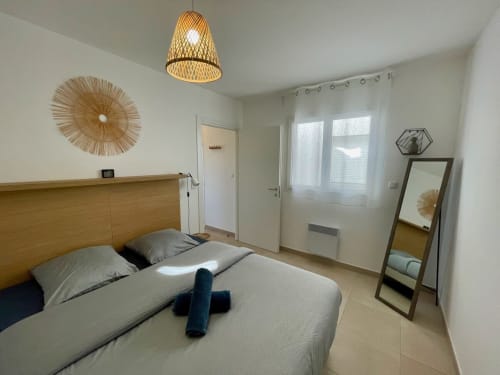 Camera moderna presso Résidence Marina di Bravone a Linguizzetta con letto in legno, lampada sospesa intrecciata e finestre con vista sul mare