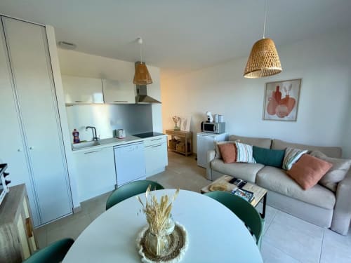 Modern T2 apartment at Résidence Marina di Bravone with open kitchen, dining table, and comfortable sofa with rattan pendant