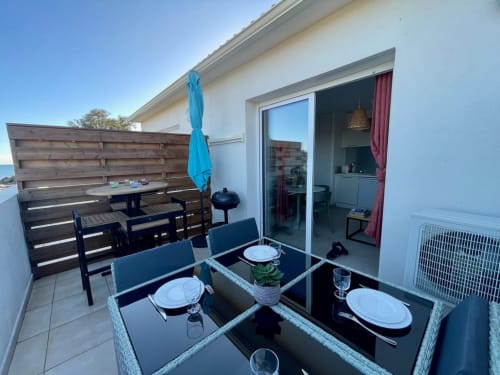 Beachfront terrace at Résidence Marina di Bravone with dining table, blue umbrella, and sea views in Linguizzetta