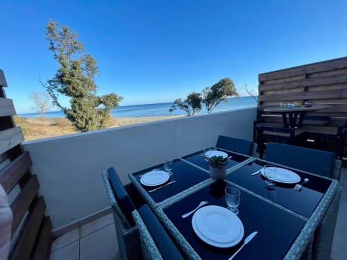 Beachfront terrace at Résidence Marina di Bravone with set dining tables overlooking the sea and sandy beach