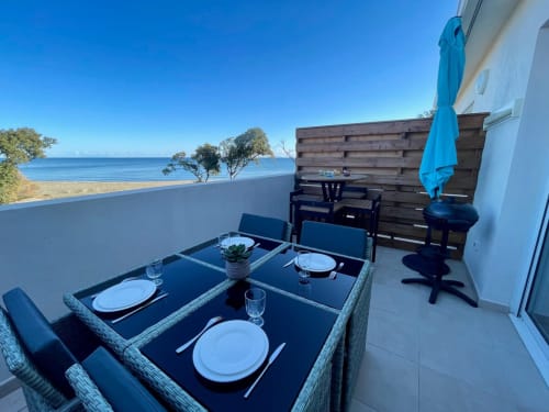 Oceanfront terrace at Résidence Marina di Bravone with set dining table, blue umbrella, and Mediterranean Sea views