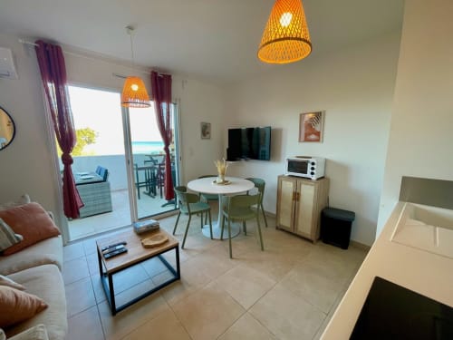 Modern apartment living room at Résidence Marina di Bravone with ocean views, dining area, and woven pendant lights