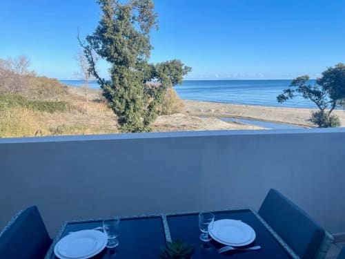 Beachfront dining at Marina di Bravone, Corsica: Table set with place settings overlooking sandy beach and blue Mediterranean