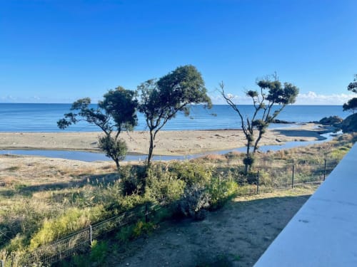 Beachfront view at Marina di Bravone, Corsica showing sandy beach, lagoon, trees and clear blue sea horizon