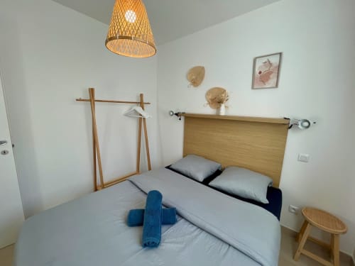 Bright bedroom at Résidence Marina di Bravone in Corsica with wooden bed, rattan pendant light, and minimalist decor