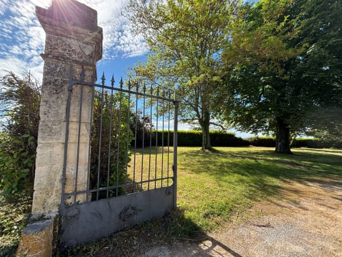 Portail en fer forgé historique à l'entrée du Château Alto Cormeil à Saint-Émilion, avec jardins soignés et allée bordée d'arbres