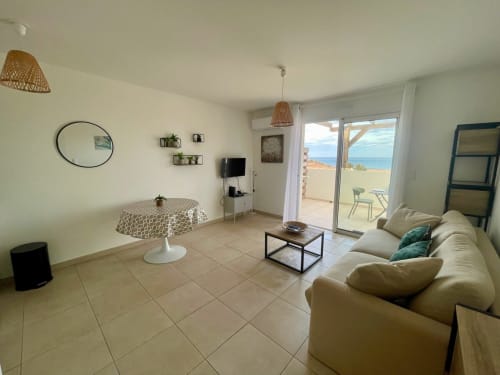 Luminoso monolocale alla Résidence Marina di Bravone con balcone vista mare, divano beige, specchio tondo e design moderno