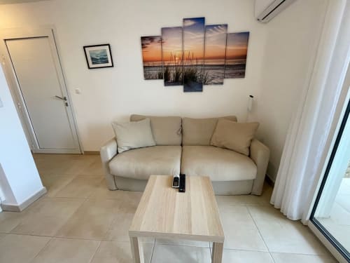 Beige sofa with cushions in Marina di Bravone apartment, light wood coffee table, coastal sunset artwork