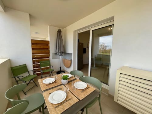 Cozy T2 apartment at Marina di Bravone with dining area, green chairs, and sliding glass doors to terrace
